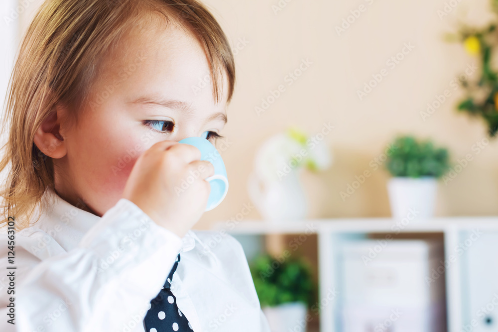 Toddler girl drinking from a mug in front of a laptop