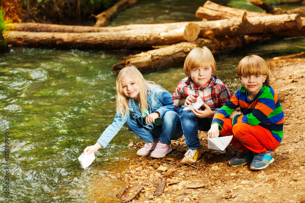 Happy kids playing with paper boats at river bank