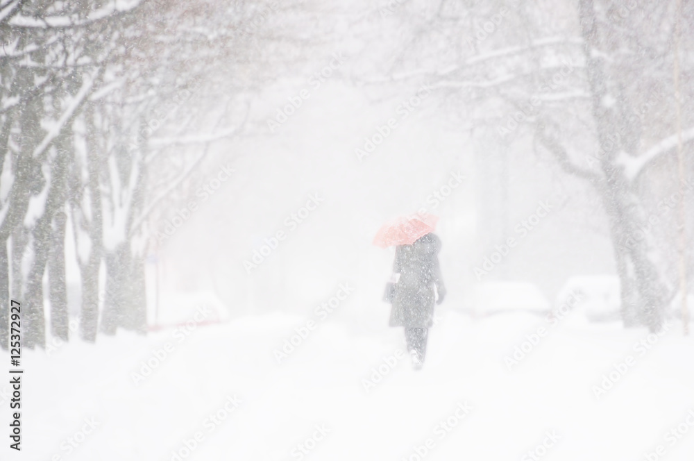 Silhouette of a woman in a dark coat with a red umbrella in a snow storm. Soft focus, blurred outlin