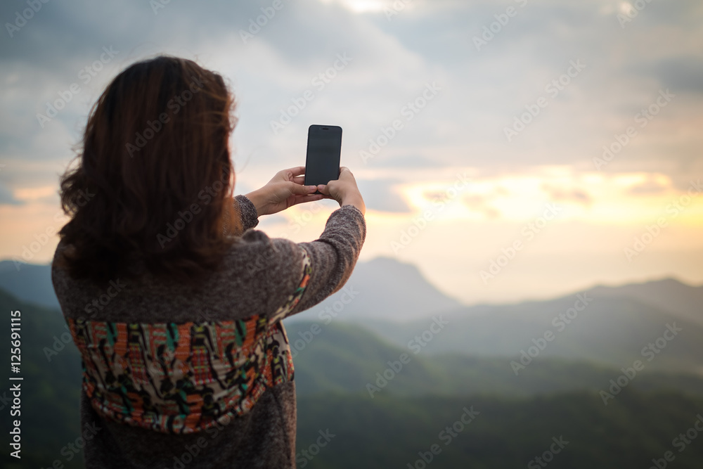 Young woman take photo of mountain view by smart phone in morning.