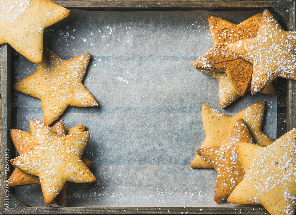 Sweet Christmas holiday gingerbread cookies in shape of stars with sugar powder on baking paper in r