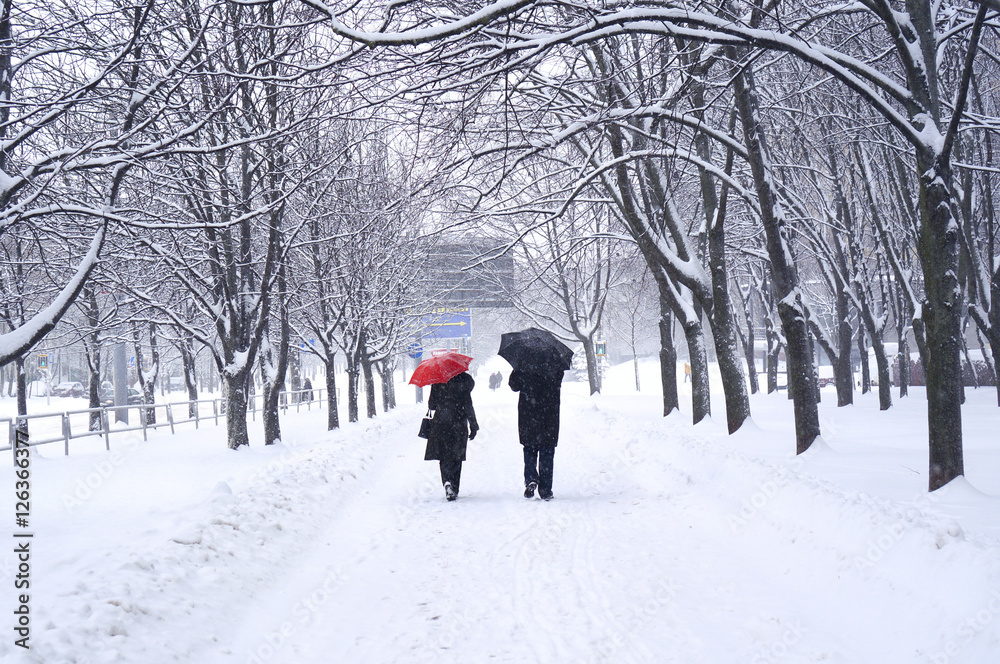 一男一女成年后，打着红黑相间的雨伞，在冬雪中走在街上。