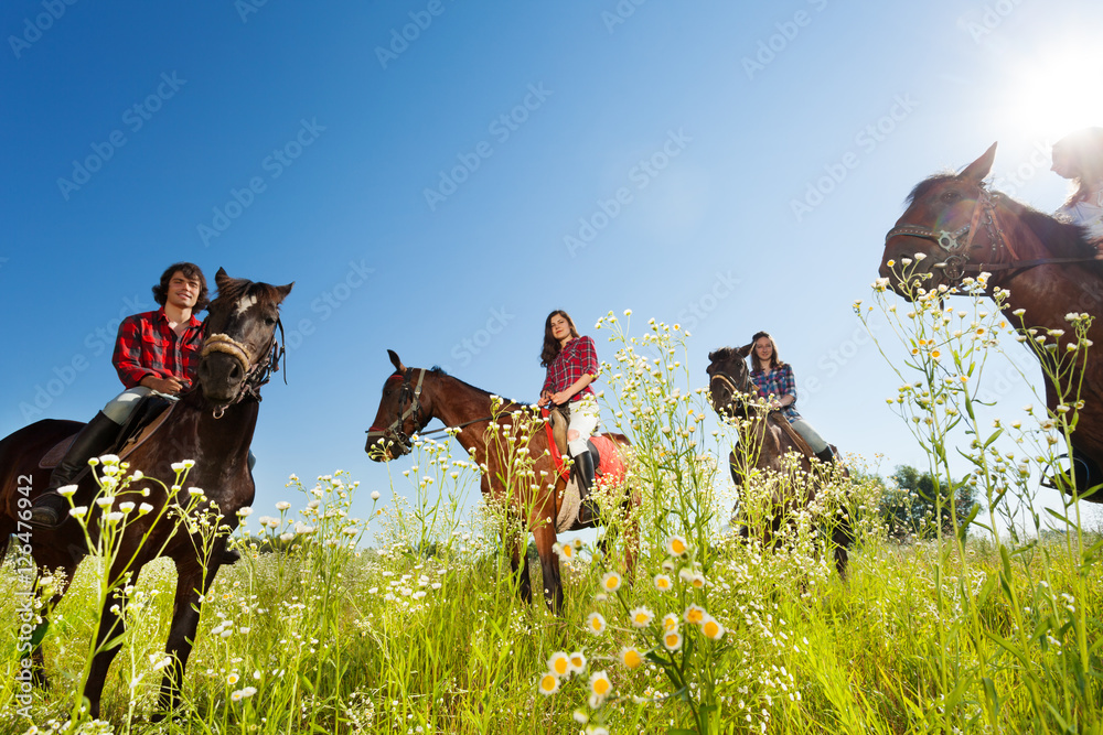 Happy equestrians riding bay horses in the meadow