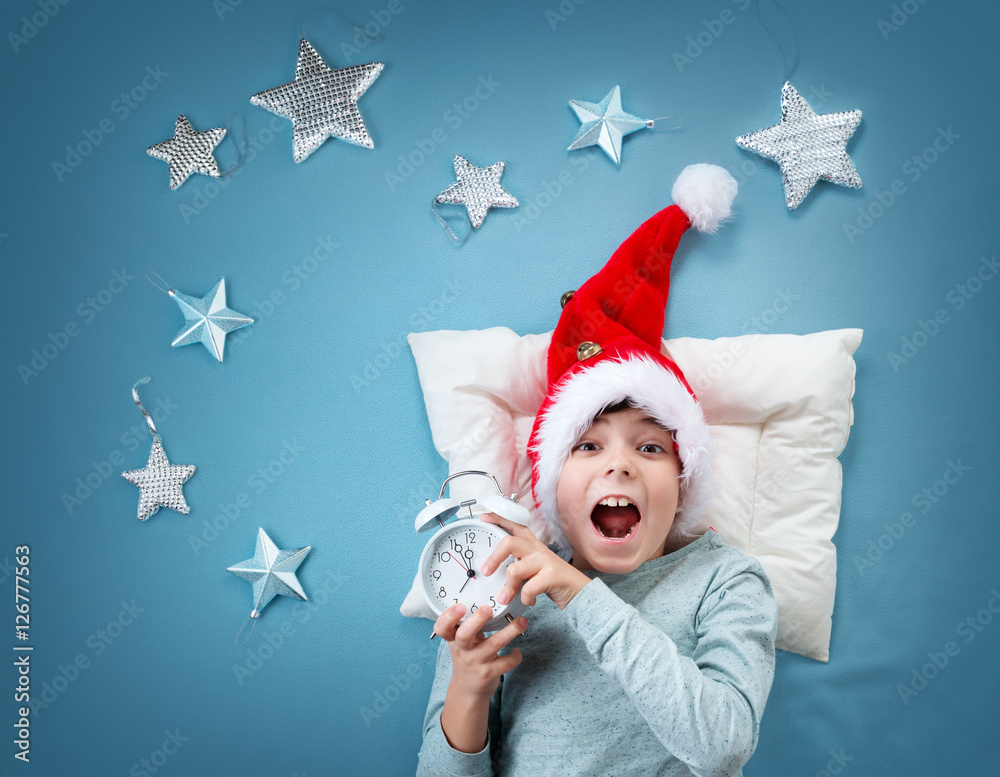 Happy child on blue blanket in red hat. Cute boy in christmas cap with alarm clock