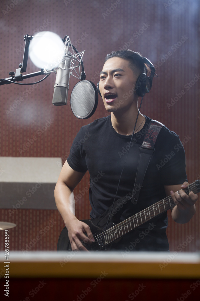 Young man singing with guitar in recording studio