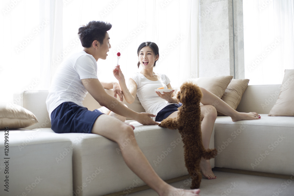 Happy young couple eating fruit salad on sofa