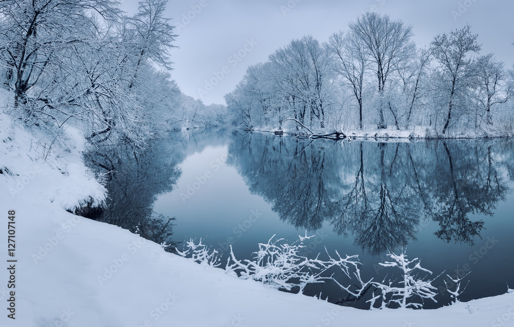 Winter forest on the river at sunset. Colorful landscape with snowy trees, beautiful frozen river wi