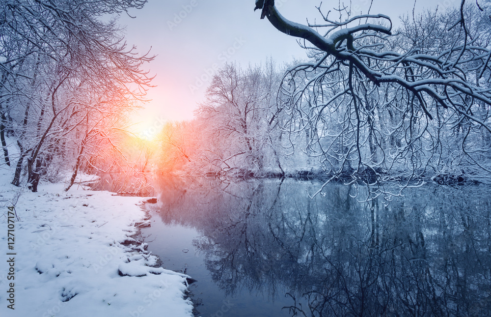 Winter forest on the river at sunset. Colorful landscape with snowy trees, beautiful frozen river wi