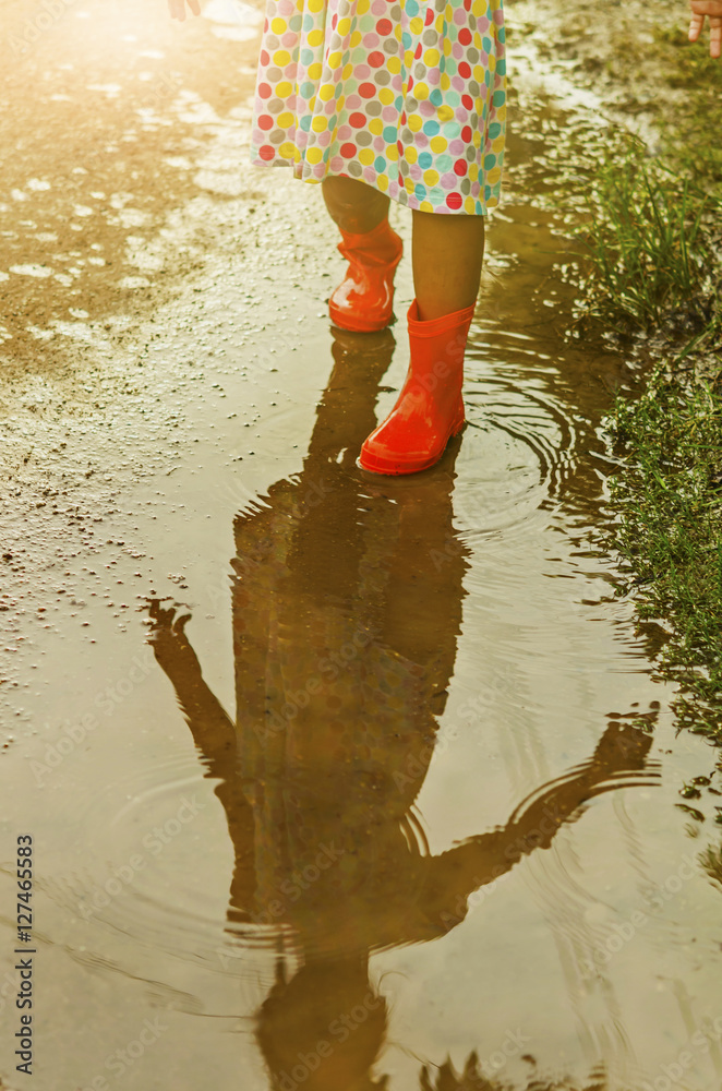 Child wearing orange rain boots walking into a puddle. Close up