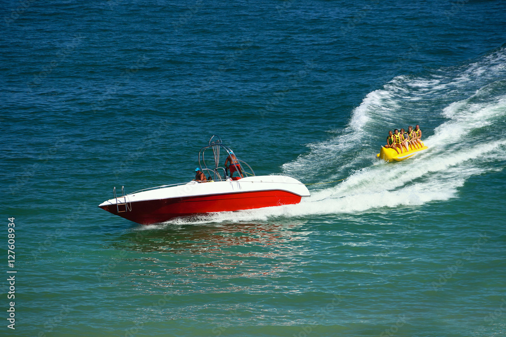 Water amusement on banana on behind a boat on a summer holiday by the sea in the resort. Beautiful b