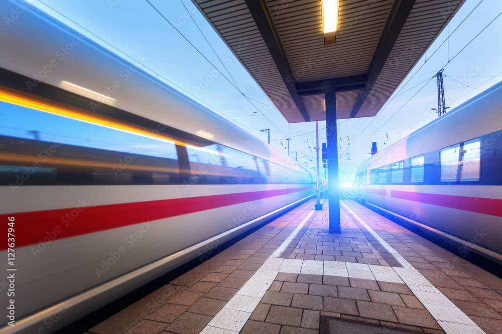 High speed passenger trains on railroad platform in motion at dusk. Blurred train. Railway station a