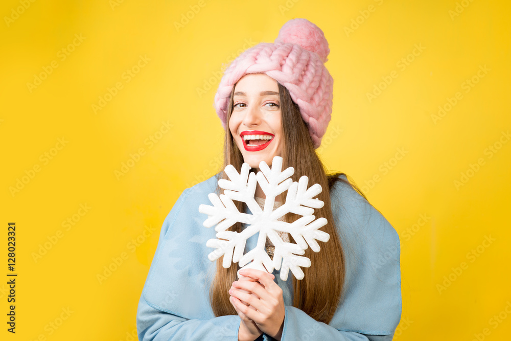 快乐的女人，穿着五颜六色的冬装，手里拿着一朵美丽的雪花，站在黄色的背上