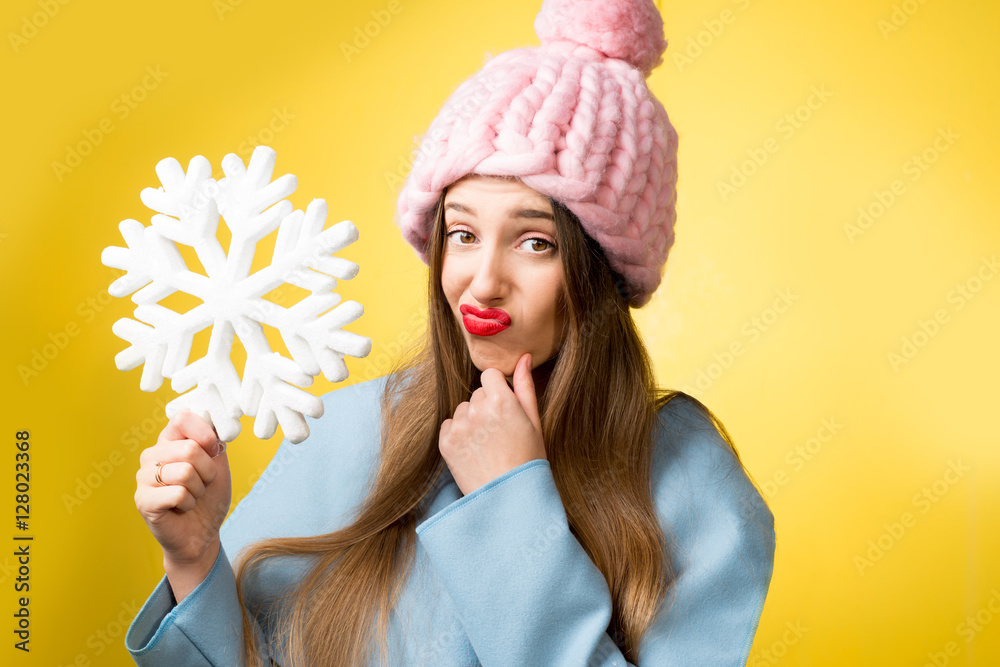 困惑而不快乐的女人穿着五颜六色的冬装，黄色背景上拿着一片雪花