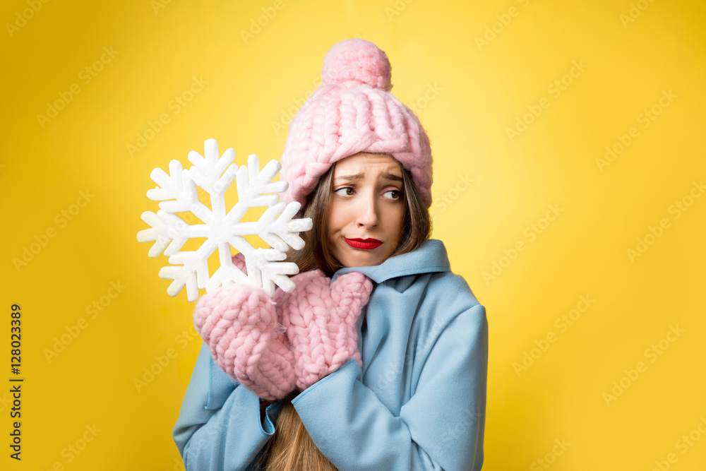 困惑而不快乐的女人穿着五颜六色的冬装，黄色背景上拿着一片雪花