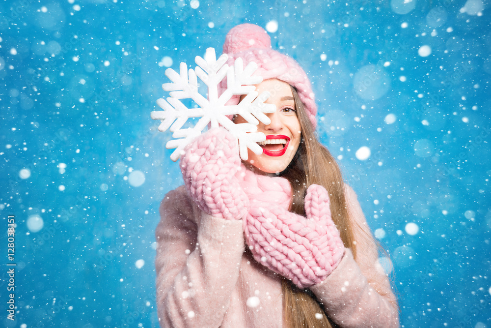 Winter portrait of a beautiful woman in knitted pink scurf, gloves and hat with snow flake on the bl