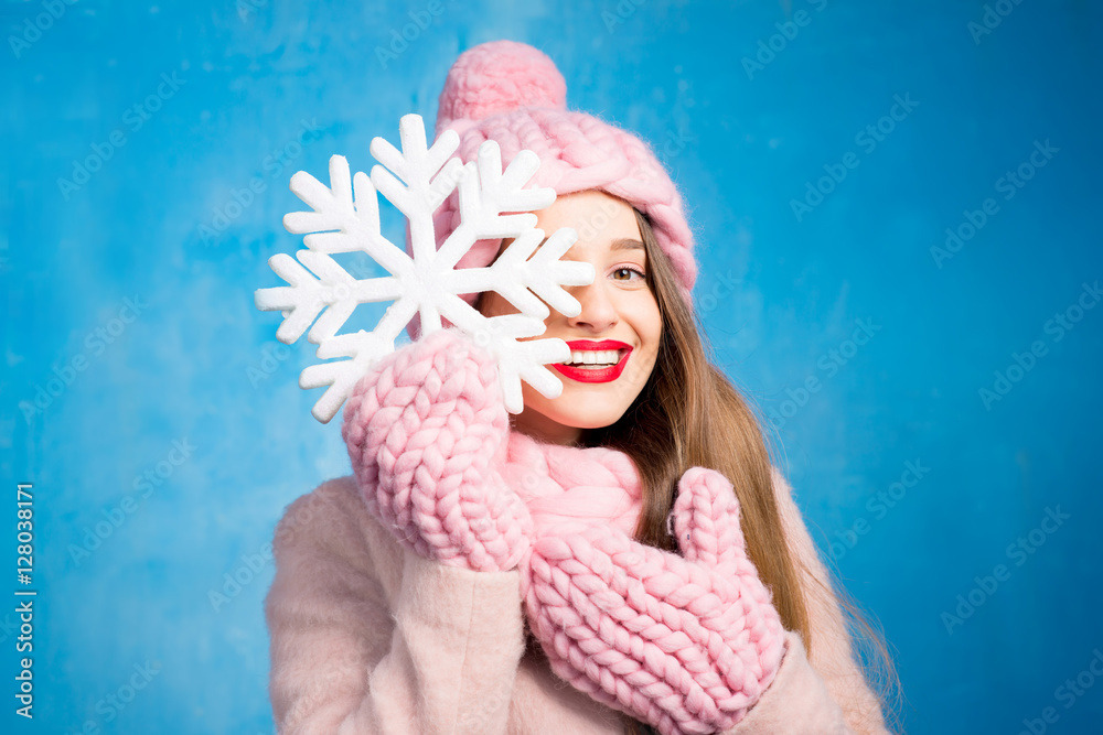 Winter portrait of a beautiful woman in knitted pink scurf, gloves and hat with snow flake on the bl