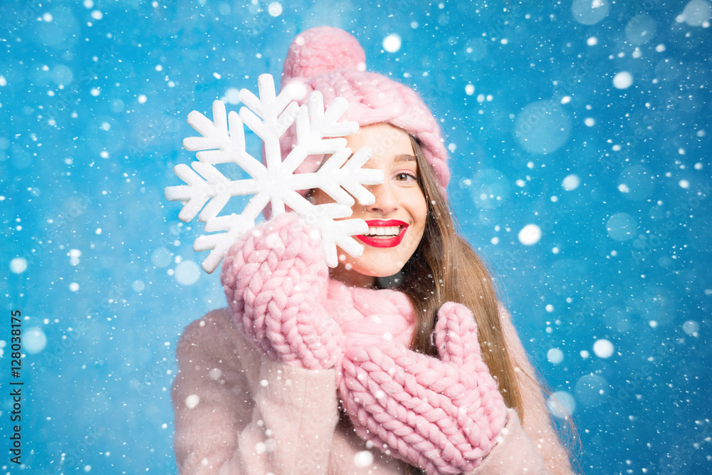 一位穿着针织粉色皮屑、手套和帽子的美女的冬季肖像，帽子上有雪花