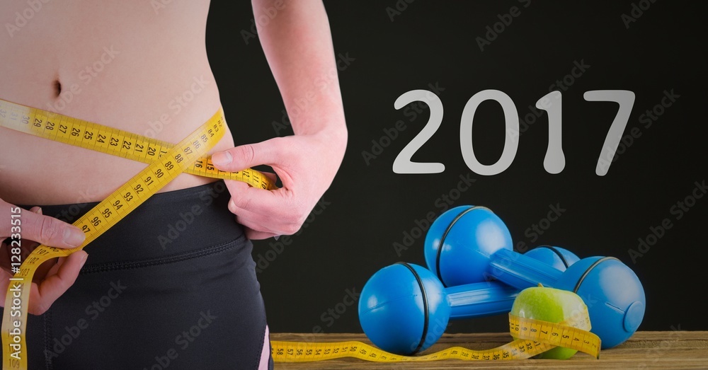 Mid section of woman measuring her waist against 2017