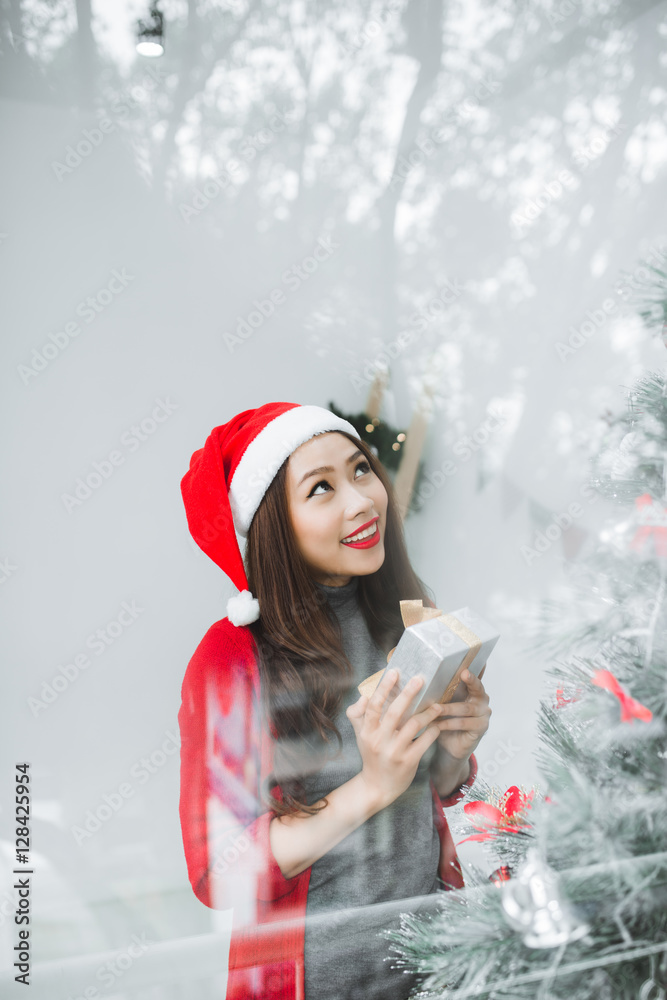 快乐的年轻亚洲女人在圣诞树旁打开购物袋