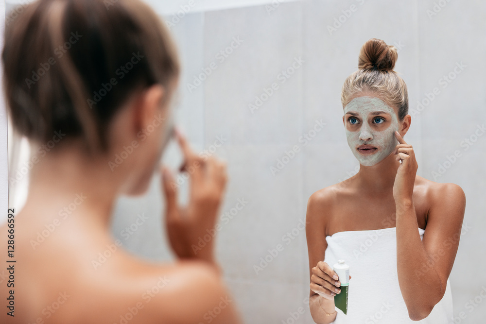 Young woman applying facial mask