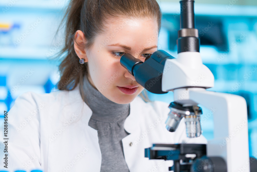 Young woman in biological laboratory. Attractive young female scientis. Scientist using a microscope