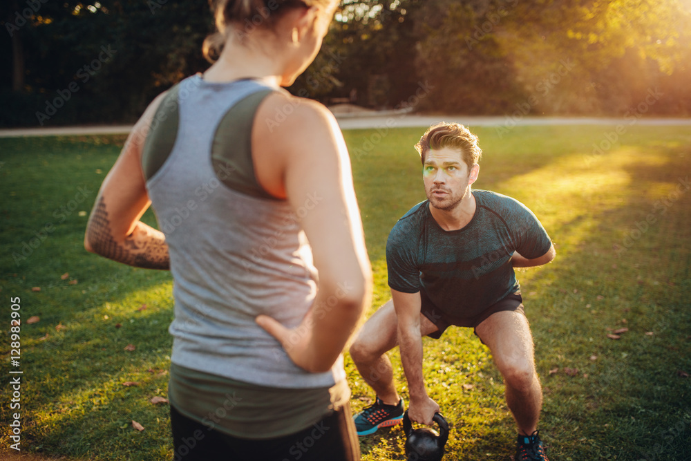 Personal trainer with man doing weight training in park