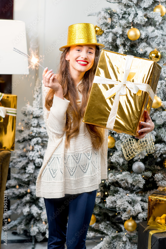 Young smiling woman in sweater and golden hat holding a gift box celebrating winter holidays with Be