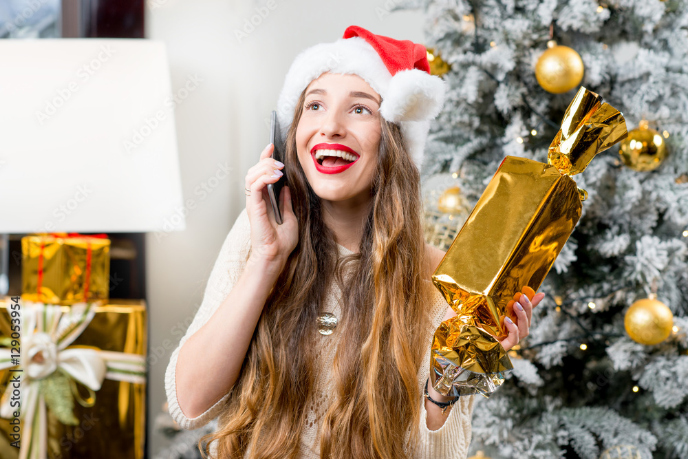 Young smiling woman in knitted hat and gloves holding a gift box celebrating winter holidays in the 