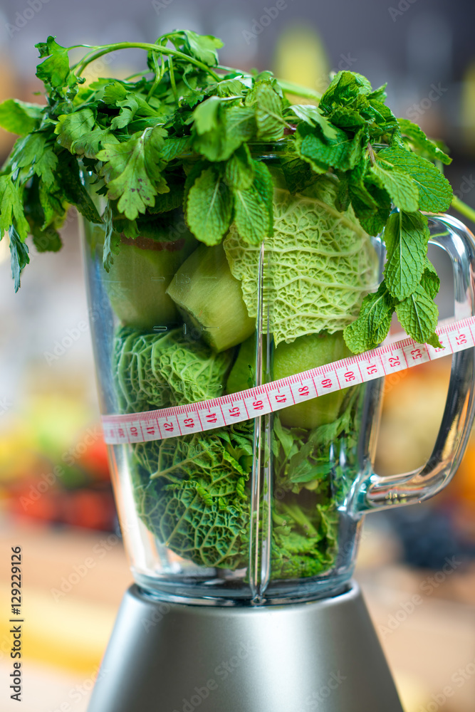 Close up view on the blender full of green fruits and vegetables ready to mix with meter in the kitc