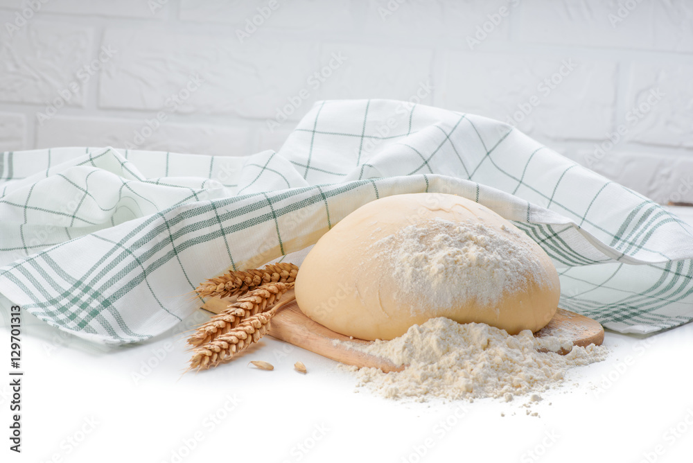 Ball of raw dough on white wooden table with ears wheat and napkin.