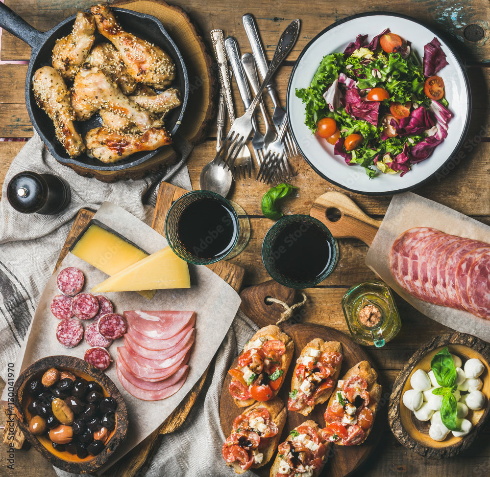 Home dinner, party table arrangement. Rustic table set with salad, olives, chicken, tomato, feta che