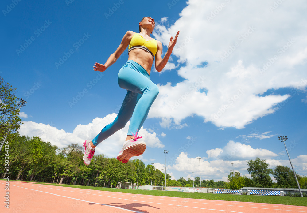 Active young woman jumping at stadium in summer