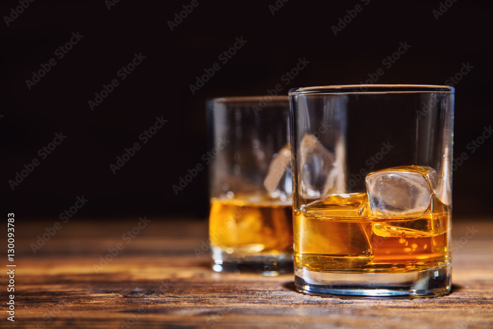 Glasses of whiskey with ice cubes served on wood