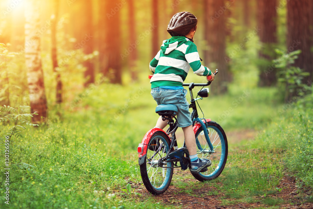 child on a bicycle in the forest in early morning. Boy cycling outdoors in helmet