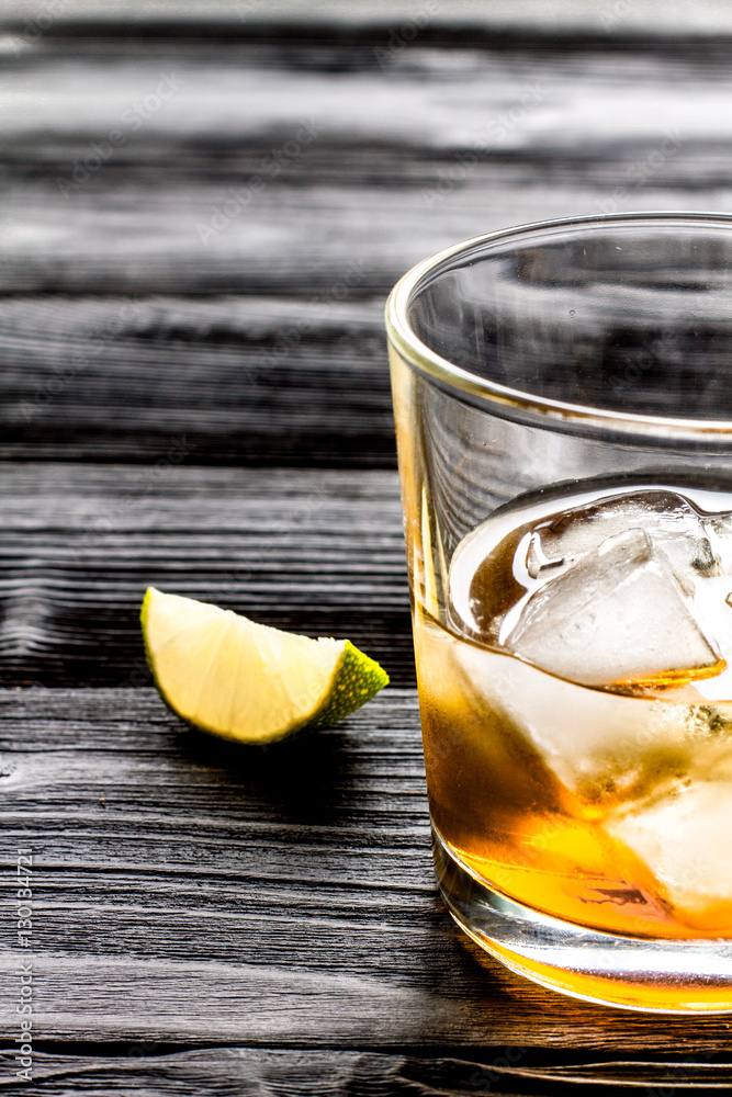 rum with ice in glass on dark background and lime