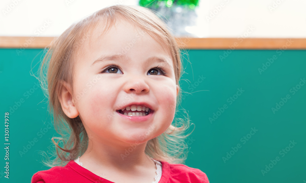 Happy toddler girl smiling in front of a chalkboard