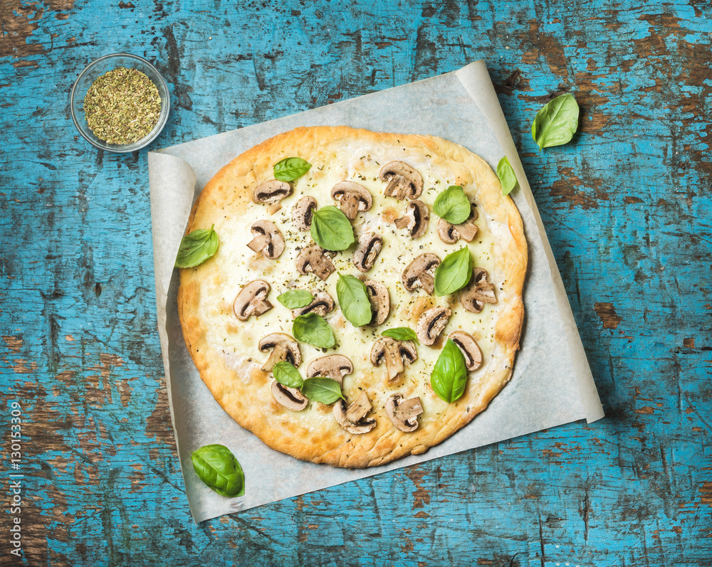 Homemade mushroom pizza with basil leaves and spices in glass on baking paper over blue rustic dark 