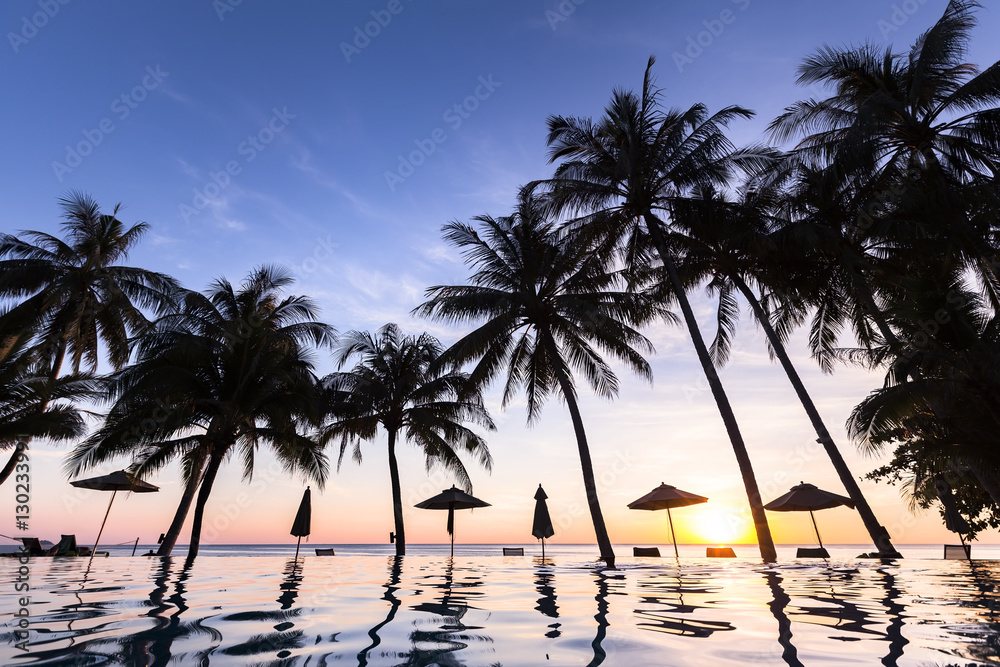 Palm trees and swimming pool at tropical resort, beach, sunset