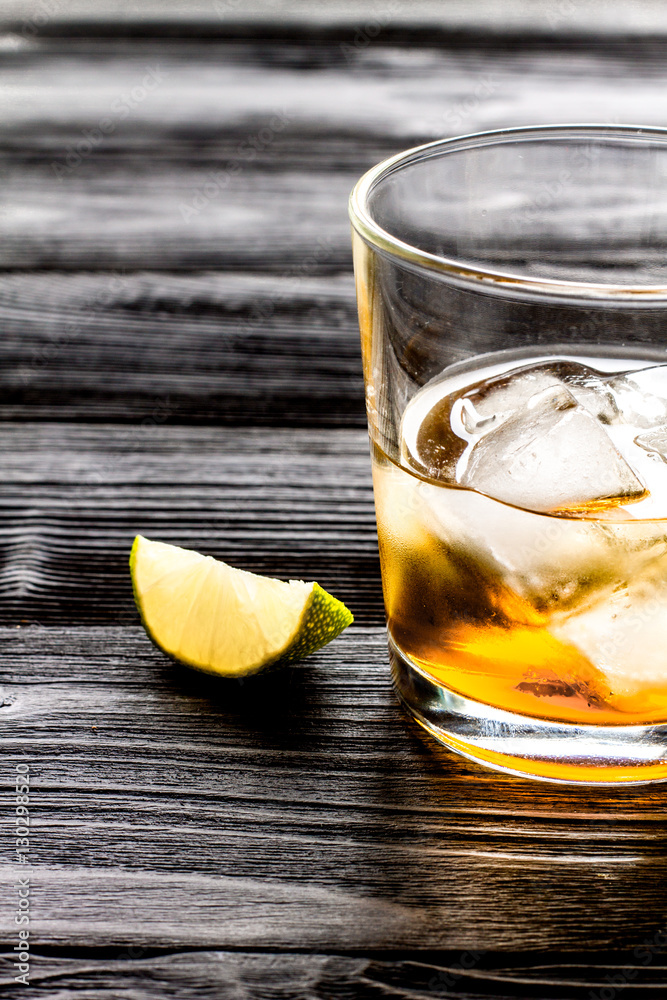 rum with ice in glass on dark background and lime