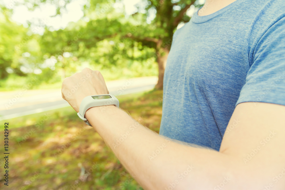 Male runner jogging outside looking at his wearable fitness tracker