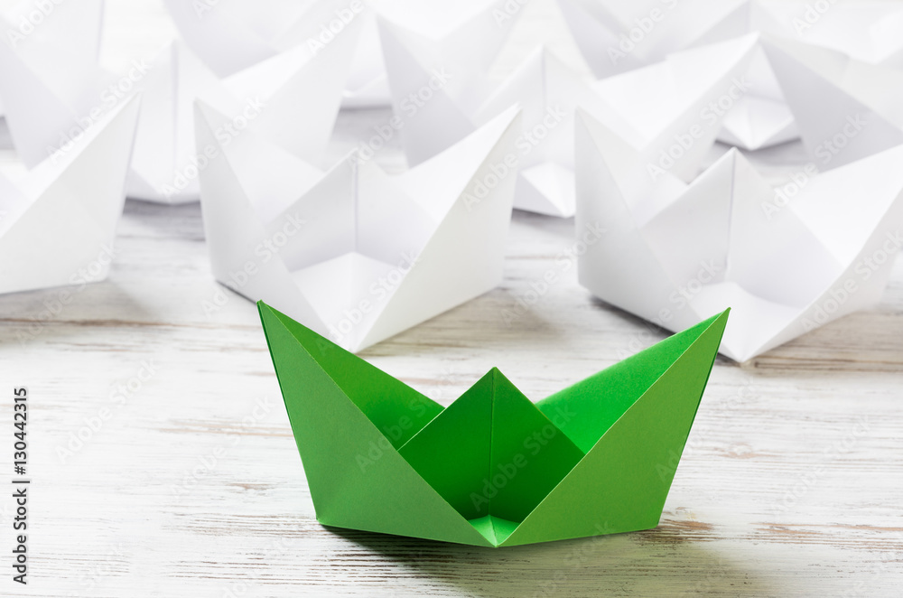 Business leadership concept with white and color paper boats on wooden table