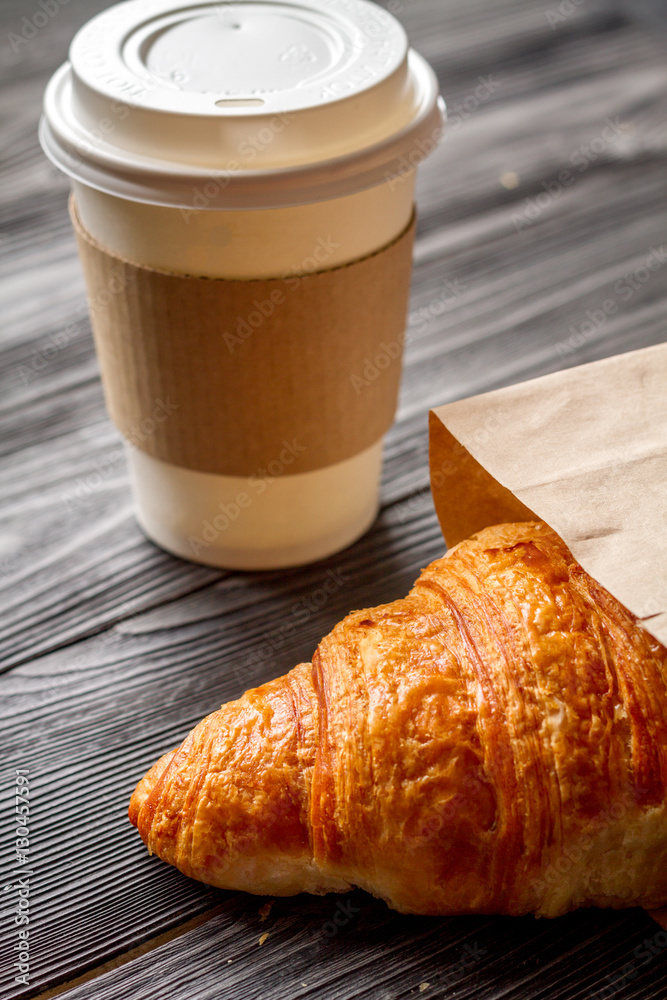 cup coffee and croissant in paper bag on wooden background