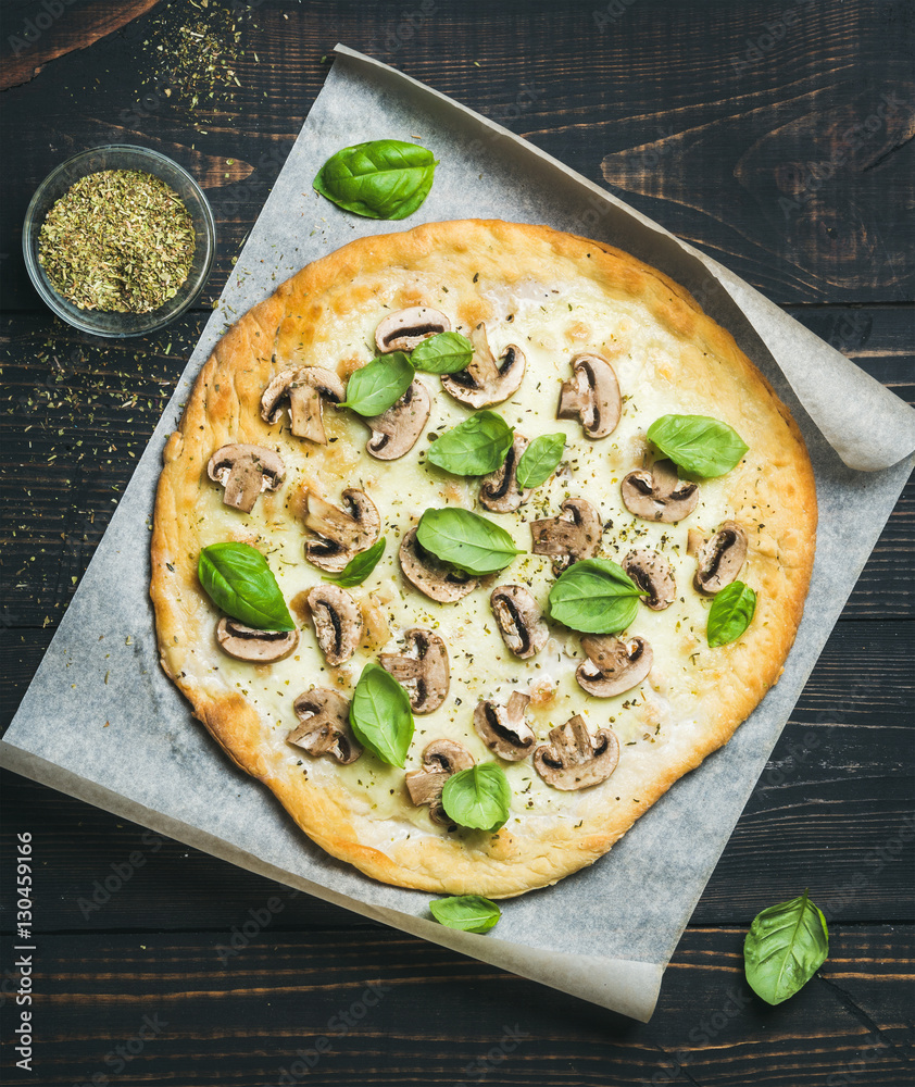 Homemade round mushroom pizza with basil leaves and spices in glass on baking paper over dark scorch