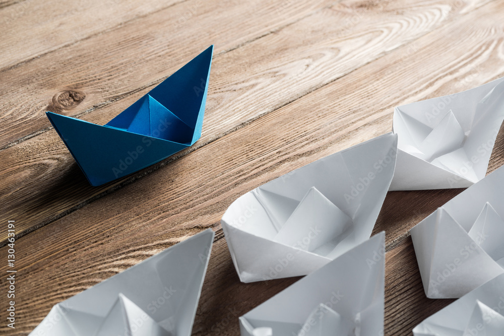 Business leadership concept with white and color paper boats on wooden table