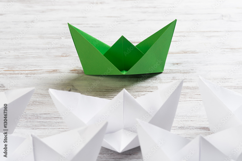 Business leadership concept with white and color paper boats on wooden table