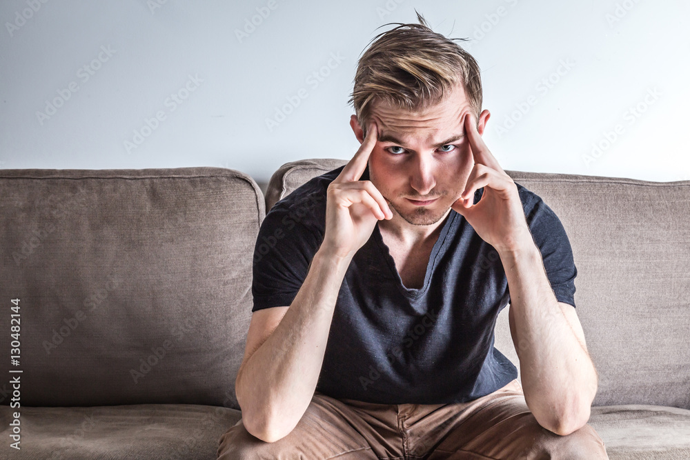 sad man in black t-shirt with a hand on the head sitting on a co