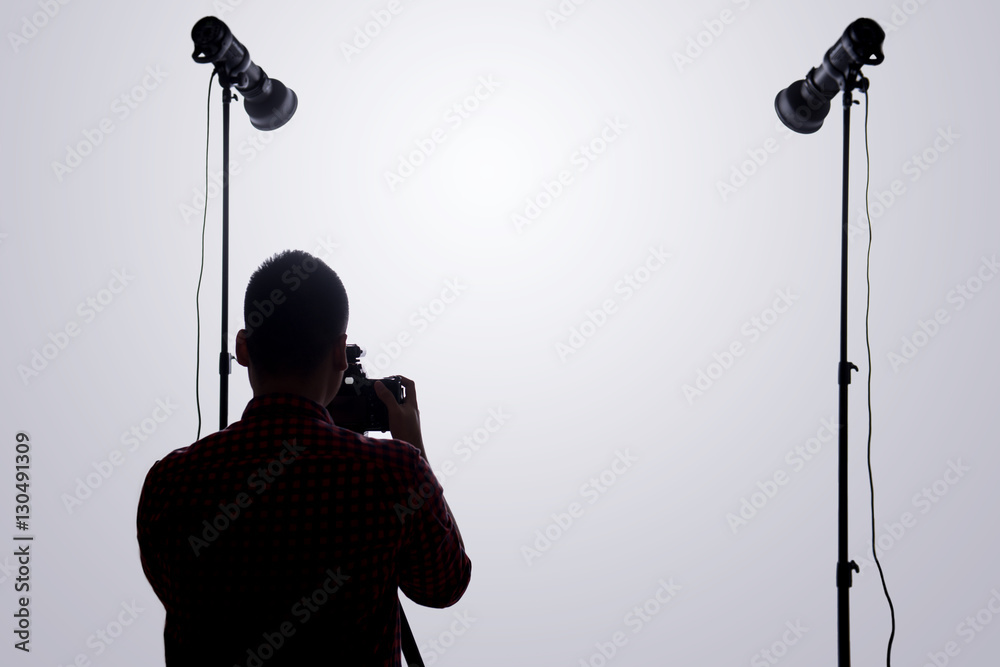 Professional photographer. Portrait of confident young man in shirt holding hand on camera while sta