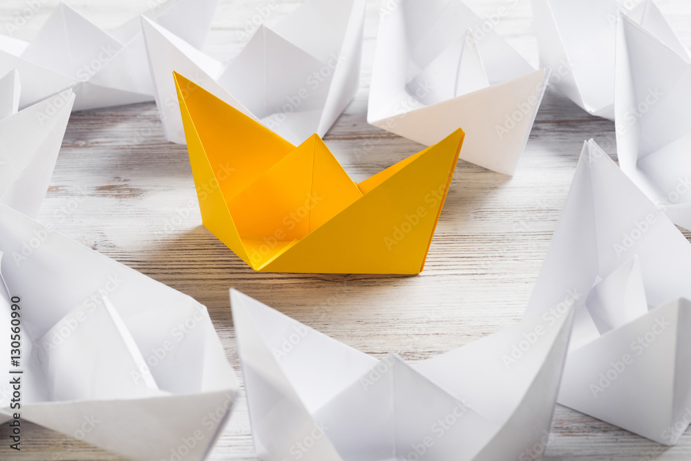 Business leadership concept with white and color paper boats on wooden table