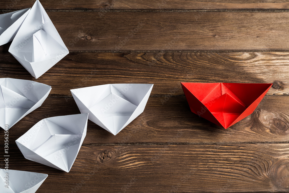 Business leadership concept with white and color paper boats on wooden table