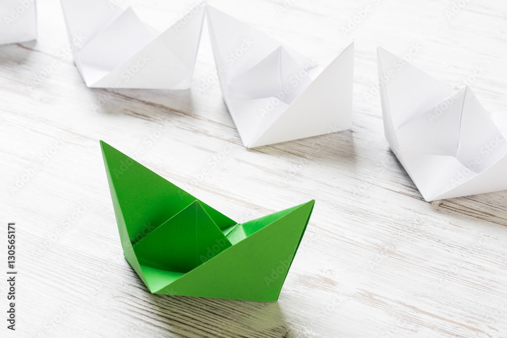 Business leadership concept with white and color paper boats on wooden table